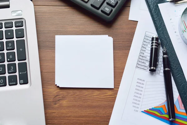 Mali yazdırılan kağıt çizelgeleri, grafikler, diyagramlar, bilgisayar, kalem ve ahşap masa hesap makinesi.