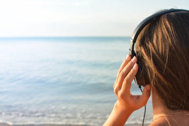 Müzik dinleme ve güzel manzaralı deniz, arka görüş zevk Kulaklığımda genç kadın.