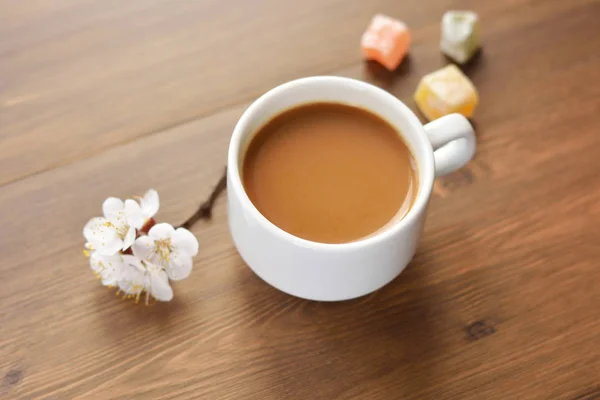 Une tasse de café chaud, des bonbons et un brin d'abricot sur une table en bois . — Photo