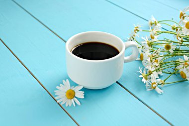 Bir fincan sıcak güçlü siyah kahve, bir buket çiçek (Papatya) mavi ahşap bir masa üzerinde. Sabah kahvaltı 