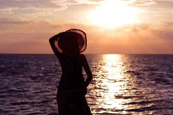 Sylweta młoda i piękna dziewczyna w kapeluszu patrząc w dal morze o zachodzie słońca (wschód) słońca. Natura i odpoczynku. Czas letni — Zdjęcie stockowe