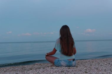 Genç güzel yalnız kız sahilde oturan ve denize mesafe içine batımını (şafak). 