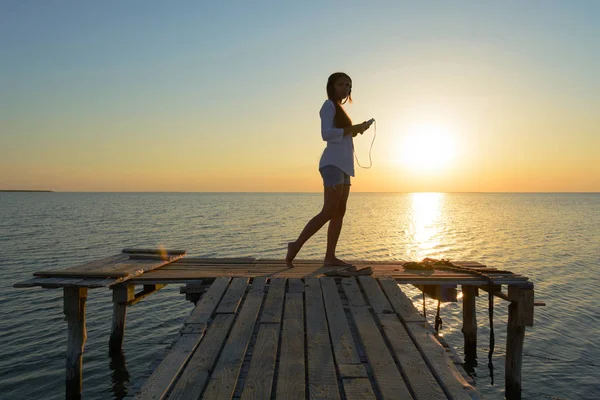 Chica en auriculares en un puente junto al mar — Foto de Stock