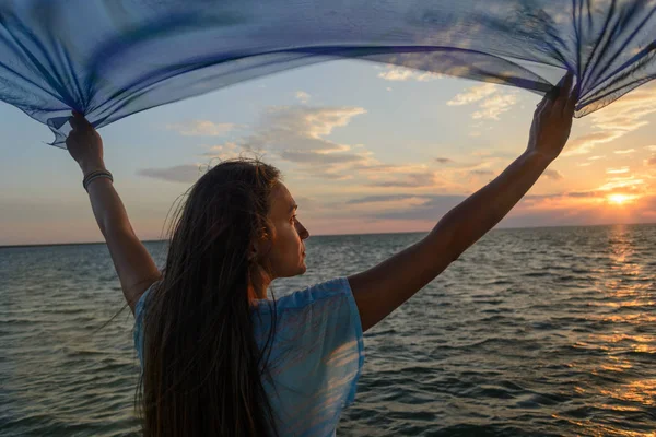 Una joven esbelta está parada en un puente de madera (puente de pesca) extendiendo sus manos sobre el mar y mirando el atardecer (amanecer) del sol. Vida y libertad . — Foto de Stock