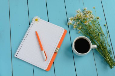 Turuncu bir dizüstü bilgisayar (bir kutu içinde a defter), chamomiles bir buket, bir kalem ve bir fincan sıcak kahve bir rure üzerinde arka plan mavi. Sanat ve yaratıcılık.
