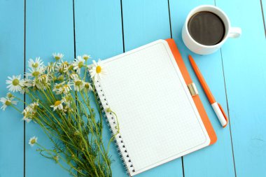 Turuncu bir dizüstü bilgisayar (bir kutu içinde a defter), chamomiles bir buket, bir kalem ve bir fincan sıcak kahve bir rure üzerinde arka plan mavi. Sanat ve yaratıcılık.