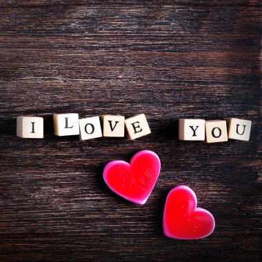 Çiğneme paketlenmiş şekerlemeler kalp şeklinde ve kelime küpleri, ahşap arka plan seni seviyorum. Metniniz için boş alan.