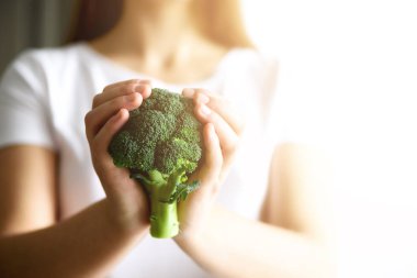 Kadın elinde beyaz T-shirt holding brokoli de. Uzay kopyalayın. Sağlıklı temiz Detoks Beslenme kavramı. Vejetaryen, vegan ham kavramı. Güneş ışığı ile tonda etkisi