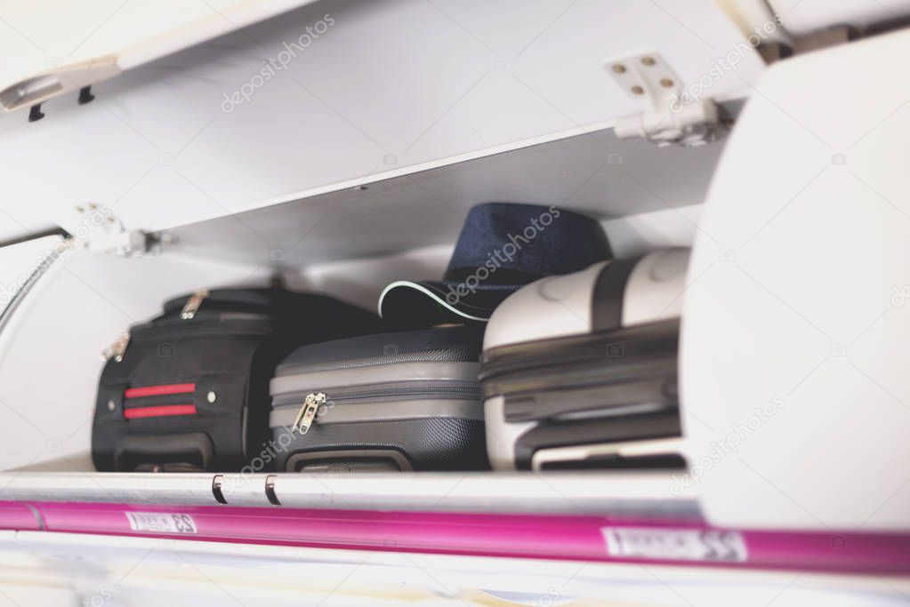 Hand-luggage compartment with suitcases in airplane. Carry-on luggage on top shelf of plane. Travel concept with copy space