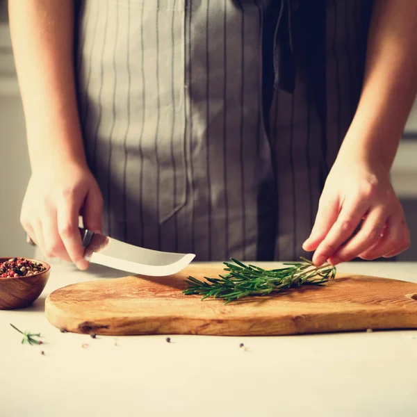 Manos de mujer cortando romero verde fresco sobre tabla de cortar de madera en la cocina blanca, interior. Copiar espacio. Comida casera engreída, receta saludable. Llévame a trabajar. — Foto de Stock