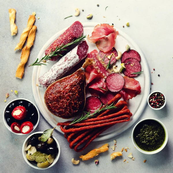 Piatto di carne affumicata fredda. Antipasto tradizionale italiano, tagliere con salame, prosciutto, prosciutto, costolette di maiale, olive su fondo grigio. Vista dall'alto, spazio di copia, disposizione piatta — Foto Stock