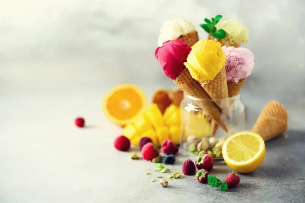 Colorful red, pink, yellow, green, white ice cream balls in waffle cones with different flavors - mango, lime, mint, pistachio, orange, strawberries, raspberries, blueberries. Summer concept — Stock Photo, Image