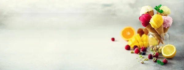 Färgglada röd, rosa, gul, grön, vit glass bollar i våffla kottar med olika smaker - mango, lime, mynta, pistage, apelsin, jordgubbar, hallon, blåbär. Sommaren koncept. Banner — Stockfoto