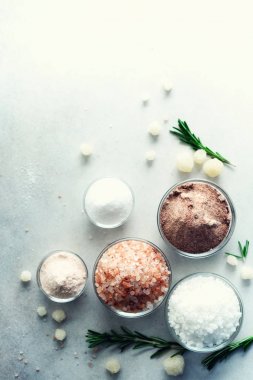 Tuz farklı gri beton zemin üzerine karışımı. Deniz tuzları, siyah ve pembe Himalaya tuz kristalleri, toz, rosemary. Ölü denizden tuz kristal toplar. Uzay kopyalayın. Üstten Görünüm.