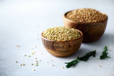 Ham organik yeşil ve ahşap kase ve biberiye gri arka plan üzerine kavrulmuş buğday. Uzay kopyalayın. Gıda katkı maddeleri.