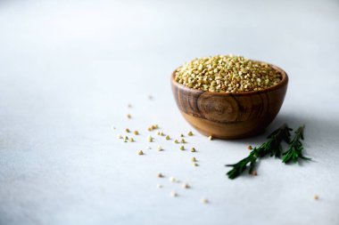 Ahşap kase ve biberiye gri arka plan üzerinde ham organik yeşil buğday. Uzay kopyalayın. Gıda katkı maddeleri.