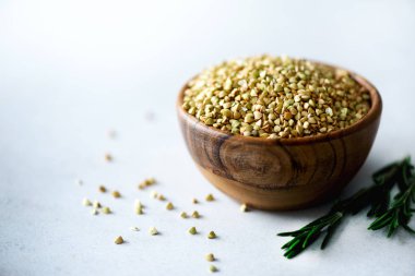 Ahşap kase ve biberiye gri arka plan üzerinde ham organik yeşil buğday. Uzay kopyalayın. Gıda katkı maddeleri.