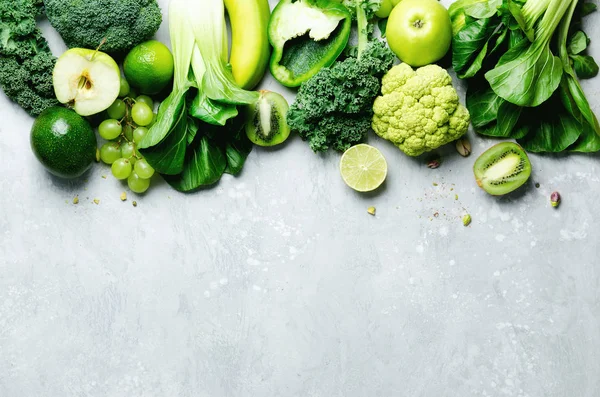 Organic green vegetables and fruits on grey background. Copy space, flat lay, top view. Green apple, lettuce, zucchini, cucumber, avocado, kale, lime, kiwi, grapes, banana, broccoli