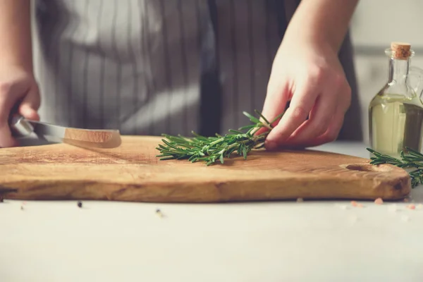 Manos de mujer cortando romero verde fresco sobre tabla de cortar de madera en la cocina blanca, interior. Copiar espacio. Comida casera engreída, receta saludable. Llévame a trabajar. — Foto de Stock