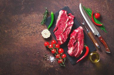 Çiğ taze et biftek domates, acı biber, sarımsak, yağ ve otlar karanlık taş, beton arka plan ile. Afiş.