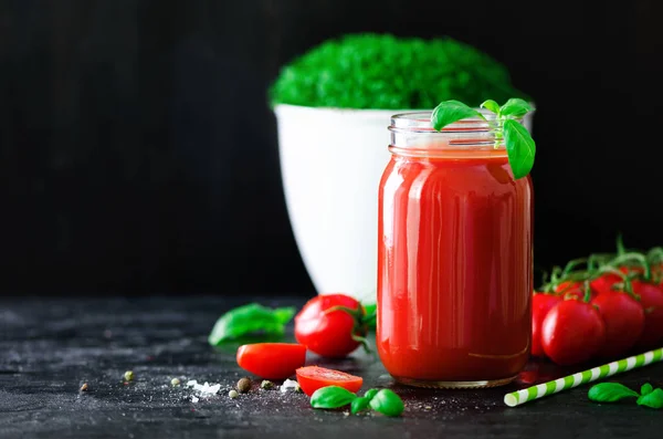 Biologische verse tomatensap in een glazen pot, basilicum, kers, zout, peper en stro op donkere zwarte achtergrond. Schoon eten en dieet concept. Kopiëren van ruimte — Stockfoto