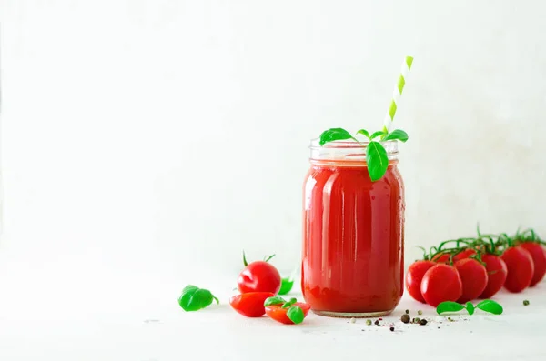 Biologische verse tomatensap in een glazen pot, basilicum, kers, zout, peper en stro op een lichte achtergrond. Schoon eten en dieet concept. Kopiëren van ruimte. — Stockfoto