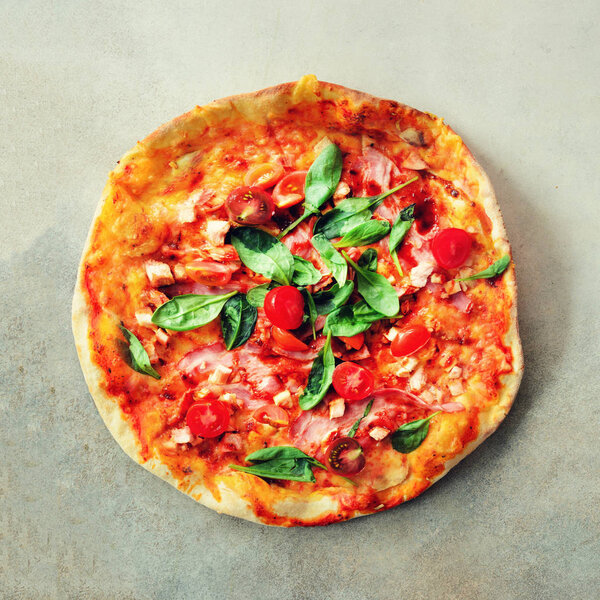 Fresh italian pizza with mushrooms, ham, tomatoes, cheese, olive, pepper on grey concrete background. Copy space. Top view. Square crop