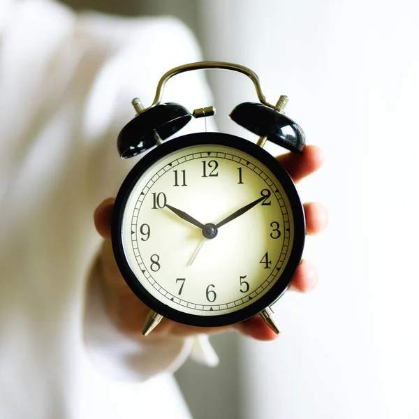 Klassisk svart väckarklocka i en hand. Solig morgonljus. Kopiera utrymme. Kvadrat gröda — Stockfoto