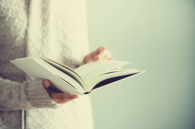 Genç kız beyaz hırka okuma kitabı açıldı. Uzay kopyalayın. yaşam tarzı ve okul kavramı