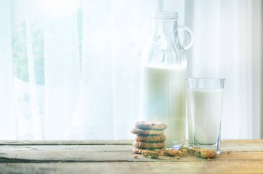 Çikolatalı kurabiye, şişe ve bardak süt pencere, beyaz arka plan yakınındaki ahşap masa üzerinde. Güneşli sabah, kopya alanı