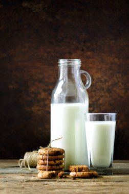 Çikolatalı kurabiye, şişe ve bardak süt ahşap masa, koyu arka plan üzerinde. Güneşli sabah, kopya alanı