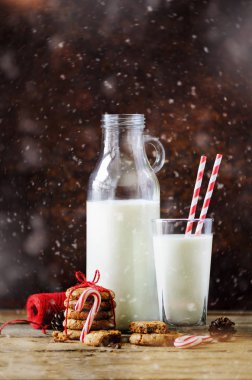 Noel koyu arka plan kar ve bokeh, kopya alanı ile. Şişe, Santa, tanımlama bilgileri, kırmızı ip, anason yıldız, tarçın, koniler, dekor ahşap antika tablo için süt ile cam.