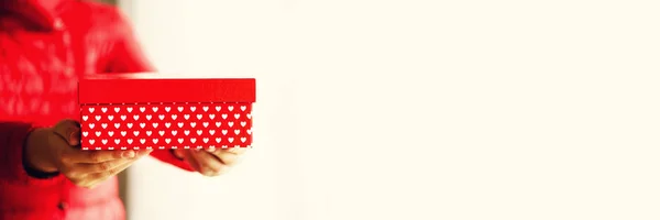 Manos femeninas sosteniendo caja de regalo roja con corazones blancos, espacio para copiar. Navidad, año hew, cumpleaños, concepto de San Valentín. Banner — Foto de Stock