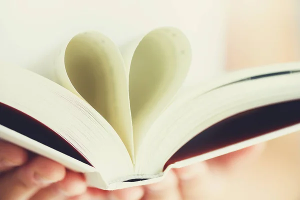 Livro com páginas abertas e forma de coração em mãos de menina. Espaço para cópia. Conceito de amor — Fotografia de Stock