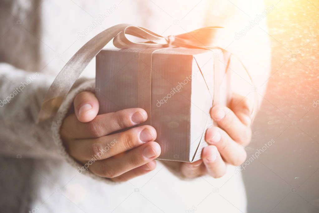 Female hands holding gift box. Copy space. Christmas, hew year, birthday concept. Festive background with bokeh and sunlight. Magic fairy tale