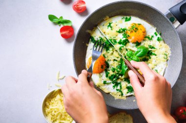 Kız ellerini üç pişmiş yumurta, otlar, peynir, domates ile kızartma tavası üzerine koy. Kadın kahvaltı yapıyor. Üstten Görünüm. Kopya alanı