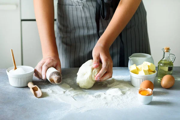 Manos femeninas amasando masa, horneando fondo. Cocinar los ingredientes - huevos, harina, azúcar, mantequilla, leche, rodillo en la cocina de estilo blanco. Copiar espacio — Foto de Stock