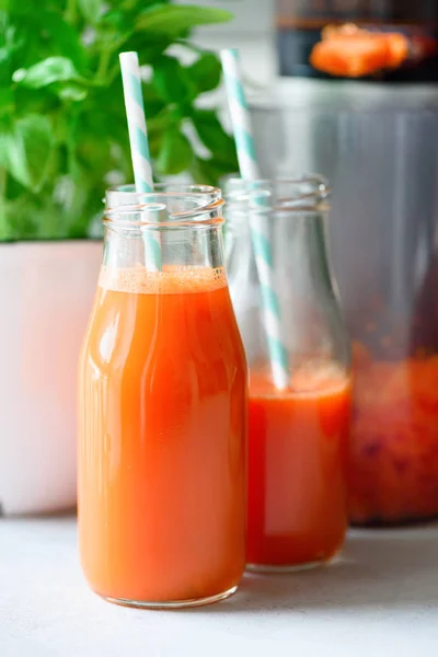 Mujer haciendo bebida fresca. Juicer y jugo de zanahoria. Frutas en el fondo. Comida limpia, concepto de desintoxicación — Foto de Stock