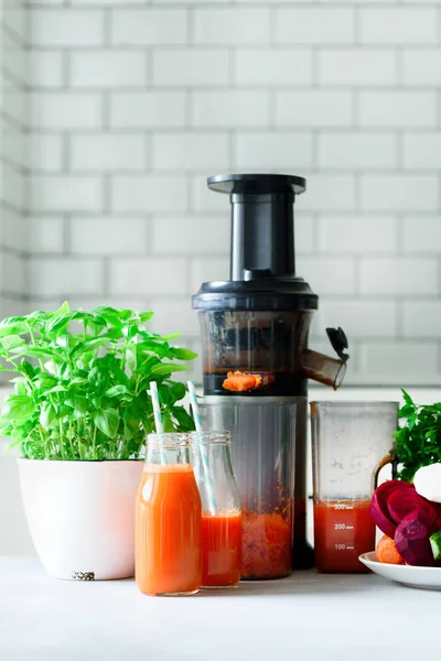 Woman making fresh drink. Juicer and carrot juice. Fruits in background. Clean eating, detox concept — Stock Photo, Image