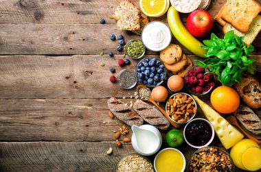 Sağlıklı kahvaltı maddeler, gıda çerçeve. Granola, yumurta, fındık, meyve, çilek, kızarmış ekmek, süt, yoğurt, portakal suyu, peynir, muz, elma ahşap rustik arka plan, üstten görünüm, kopya alanı