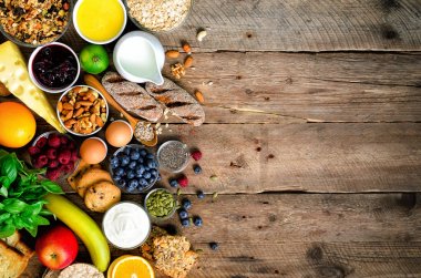 Sağlıklı kahvaltı maddeler, gıda çerçeve. Granola, yumurta, fındık, meyve, çilek, kızarmış ekmek, süt, yoğurt, portakal suyu, peynir, muz, elma ahşap rustik arka plan, üstten görünüm, kopya alanı