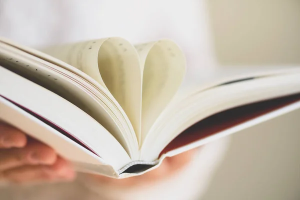 Livro com páginas abertas e forma de coração em mãos de menina. Espaço para cópia. Conceito de amor — Fotografia de Stock