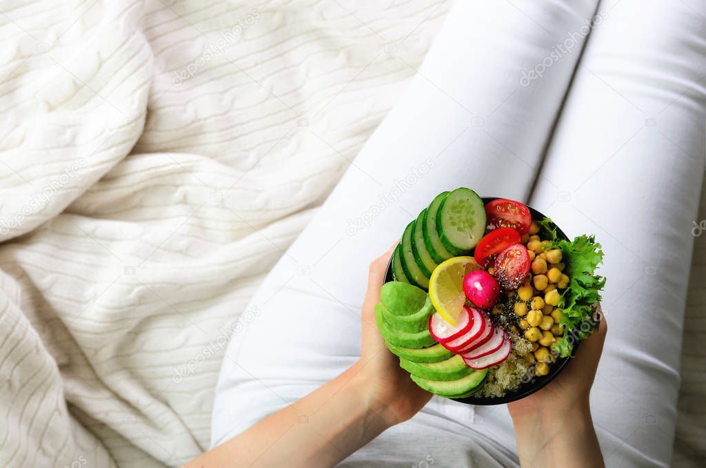 Girl holds in hands vegan, detox raw buddha bowl with avocado, quinoa, cucumber, radish, salad, lemon, cherry tomatoes, chickpea, chia seeds on textile background, copy space, overhead