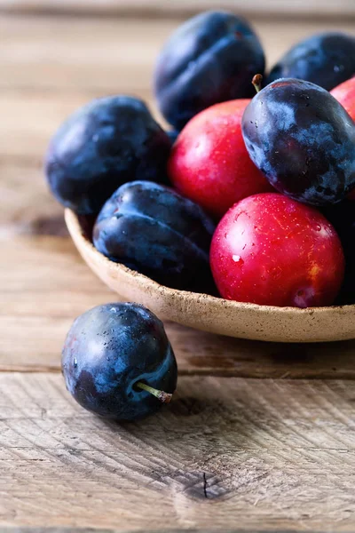 Ciruelas orgánicas azules y rosadas sobre fondo de madera oscura. Espacio de copia — Foto de Stock