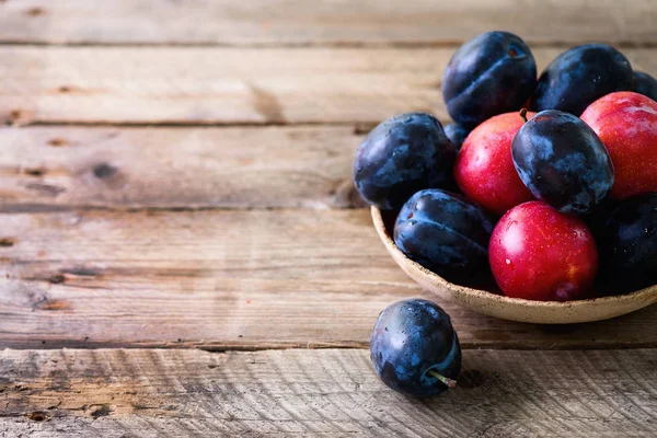 Ciruelas orgánicas azules y rosadas sobre fondo de madera oscura. Espacio de copia — Foto de Stock