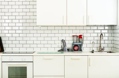 Beyaz minimalist mutfak iç ve tasarım. Döşeme duvar arka planı. Ev aletleri - blender, vakum makinesi, modern fırın, bulaşık makinesi, fırın, tablo, musluk Mikser
