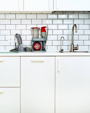 Beyaz minimalist mutfak iç ve tasarım. Döşeme duvar arka planı. Ev aletleri - blender, vakum makinesi, modern fırın, bulaşık makinesi, fırın, tablo, musluk Mikser