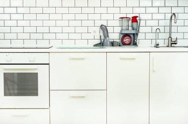 Beyaz minimalist mutfak iç ve tasarım. Döşeme duvar arka planı. Ev aletleri - blender, vakum makinesi, modern fırın, bulaşık makinesi, fırın, tablo, musluk Mikser