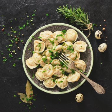 Geleneksel Rus mantı, mantı, mantı siyah beton zemin üzerine etli. Maydanoz, bıldırcın yumurtası, biber, biberiye, defne yaprağı ve baharat. Üstten Görünüm. Tonda etkisi. Boşaltmak.