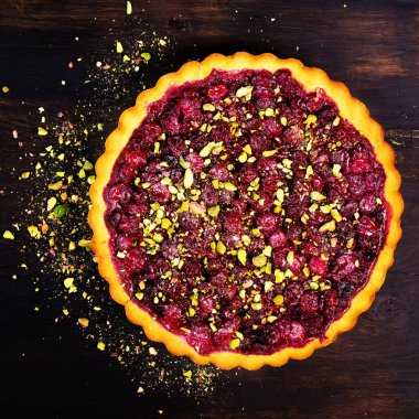 Tatlı tart ahududu, kiraz, Antep fıstığı ile kırmızı kuş üzümü ile koyu ahşap zemin üzerine pudra şekeri. Boşaltmak. Üstten Görünüm